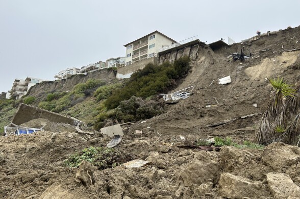 Portions of a home have broken off and slid down a hill. The sky looks gray and stormy.