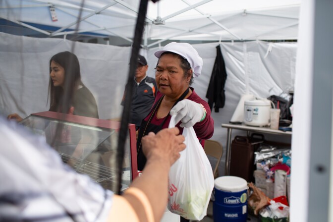 Lamduan Ruanthong hands a customer their order at thai food stall, So Zaap,  at the East Hollywood Farmer's Market on Hollywood Boulevard on June 6, 2019 in Los Angeles, California. (James Bernal for KPCC)
