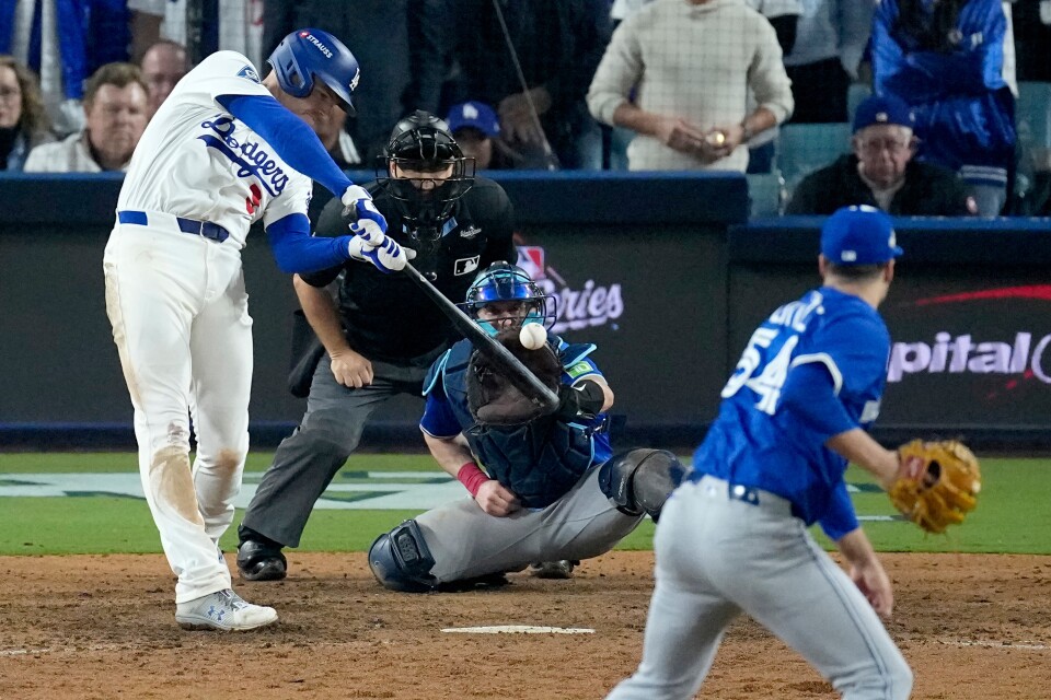 A batter in a white Dodgers uniform is swinging bat at incoming pitch.