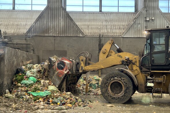 A frontloader scoops bagged food waste from the wet ground of a large warehouse. 