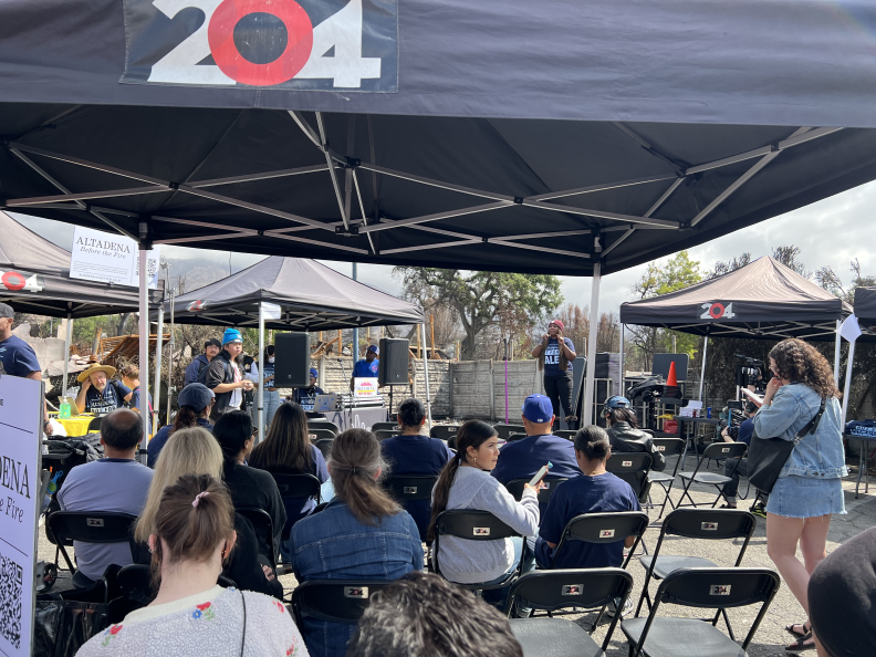 A black pop-up tent has rows of chairs with people in them.