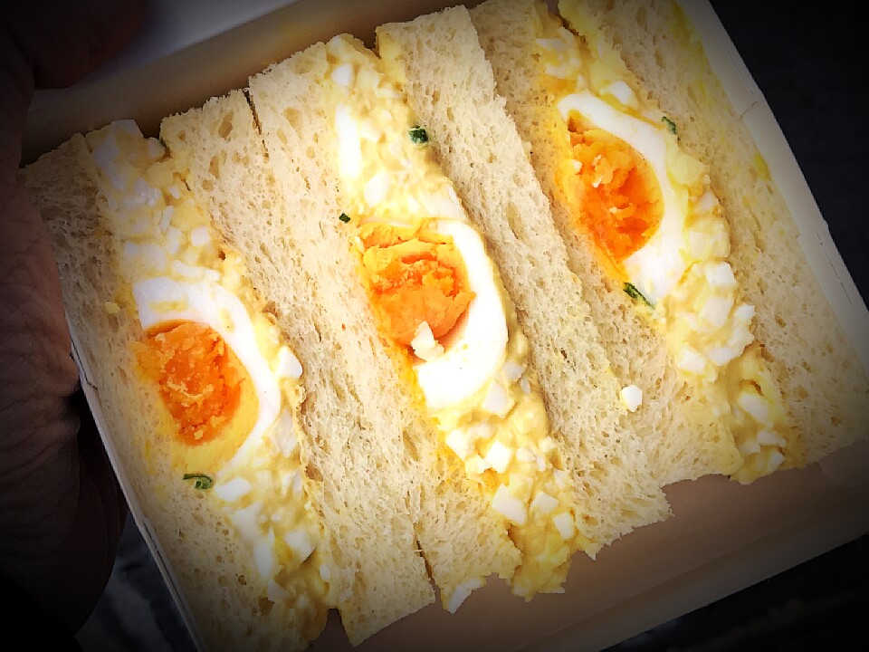 a hand holds a box with three sections of a slice egg salad sandwich