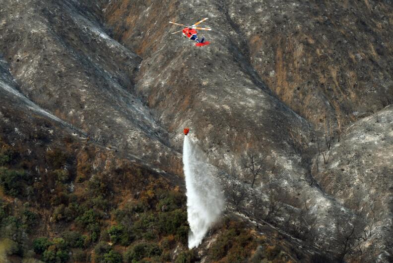 A helicopter dumps water on the a wildfire burning in the San Gabriel Mountains.
