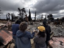 Four people stand atop the rubble of an Altadena home.