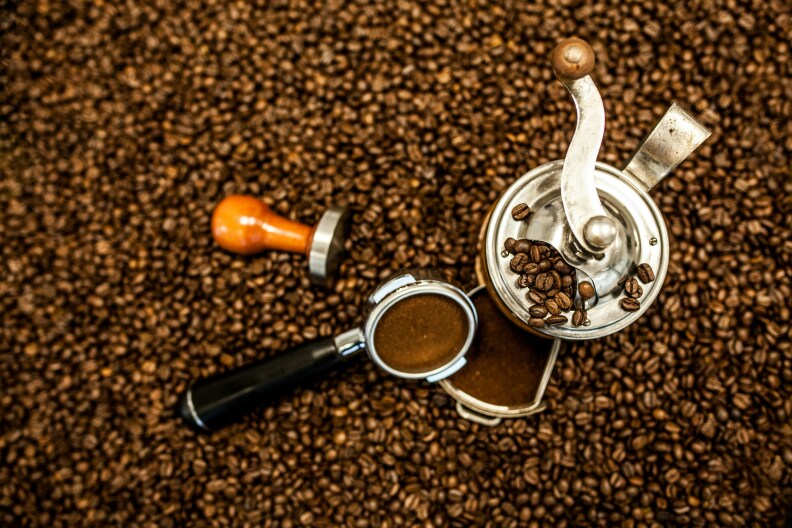 A stock photo showing a coffee press with grounds sitting atop a massive bed of coffee beans.