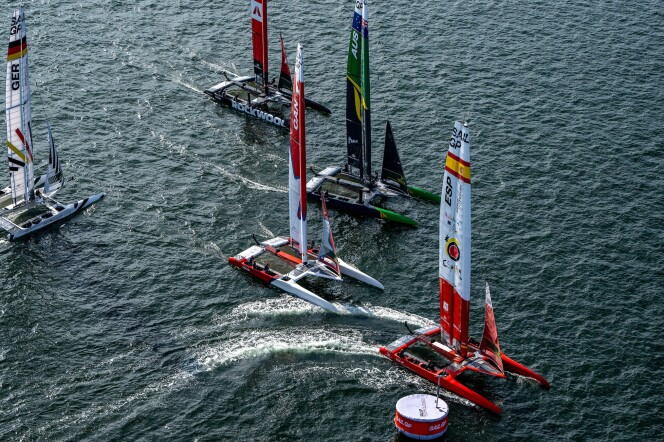Five catamarans sailing in open water during a race. They're varying colors to represent different countries, including Spain, Canada, Australia and Germany. 