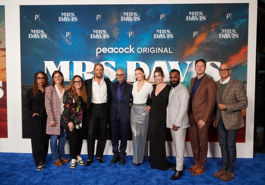 A group of 10 people stand side-by-side in front of a backdrop.