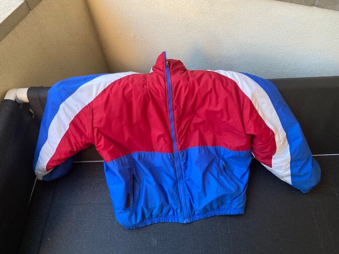 photo shows a red, white, and blue windbreaker laid out across a gray sofa.