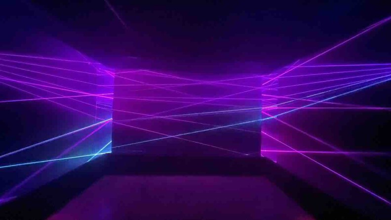 A dark room criss-crossed by purple and blue laser light streams