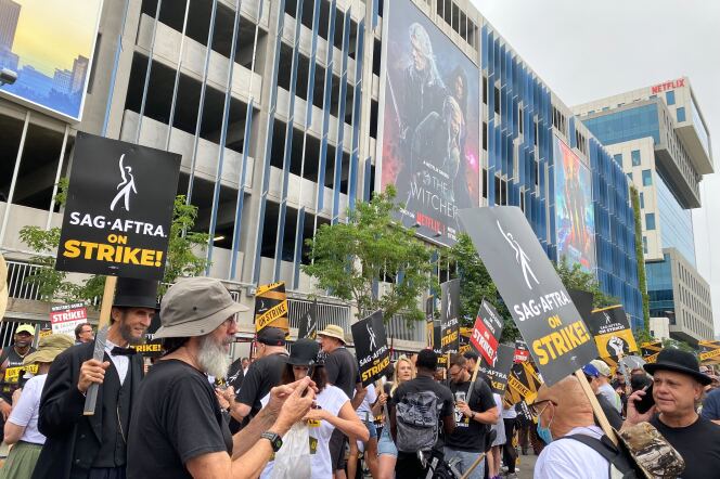 people gather on the street outside tall buildings. They're holding signs that say SAG AFTRA on strike. 