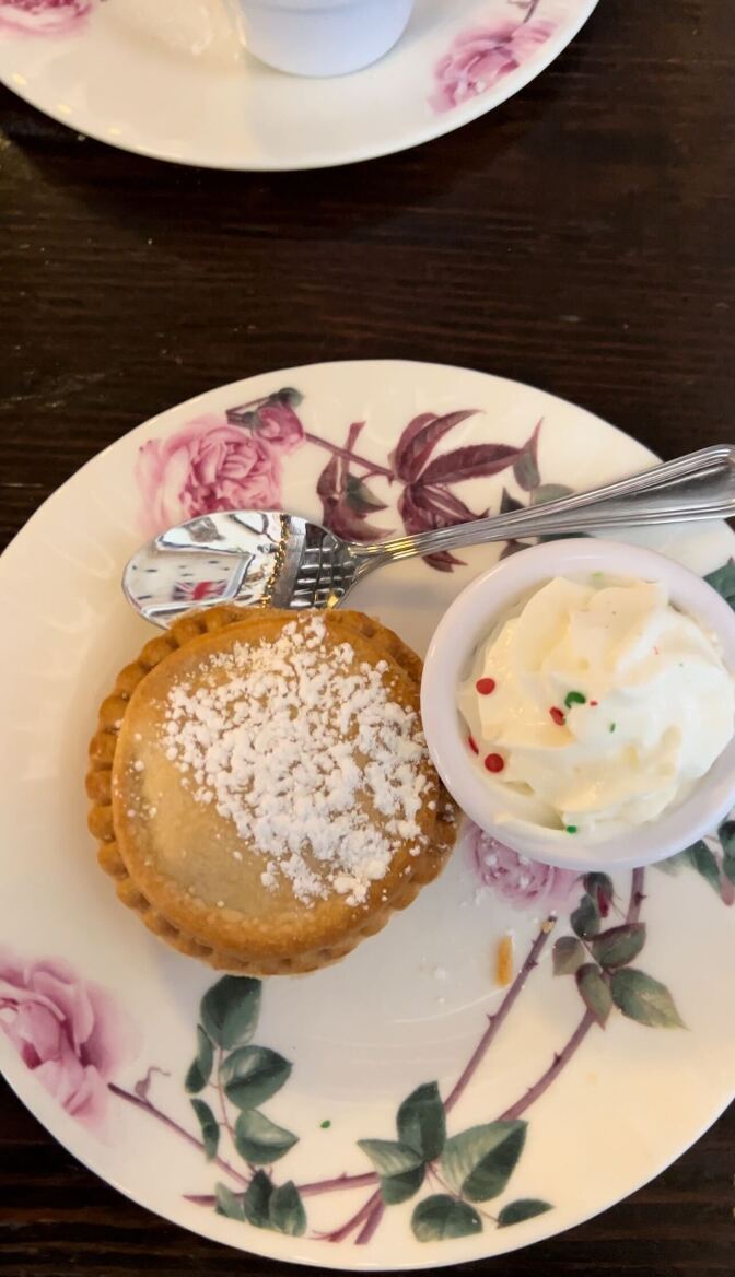 A small pastry sits on a white plate with a floral design next to a ceramic container filled with white cream.