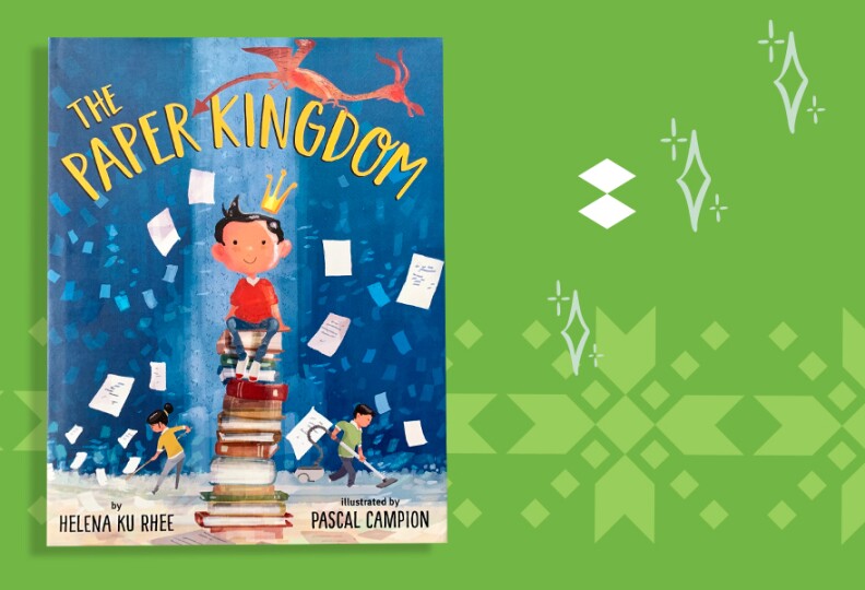 The cover of a book shows a boy with medium-light skin tone and dark hair that sticks up a bit in the front sitting on a stack of books, wearing a crown. A man and woman with similar features mop and vacuum in the background. Paper flutters int he air and a dragon flies overhead. The title reads The Paper Kingdom.