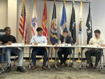 Four men sit at a table with military flags and the U.S. flag behind them. Congressman Dave Min is center-right. 