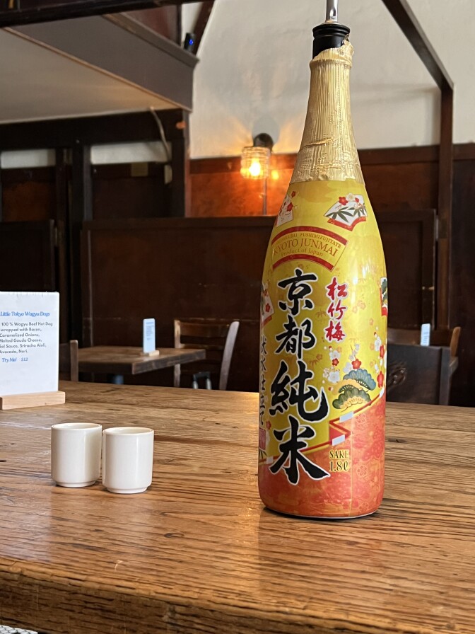 The 1.8L gold and orange bottle of Sho Chiku Bai Kyoto Junmai sake is seen next to two sake glasses.