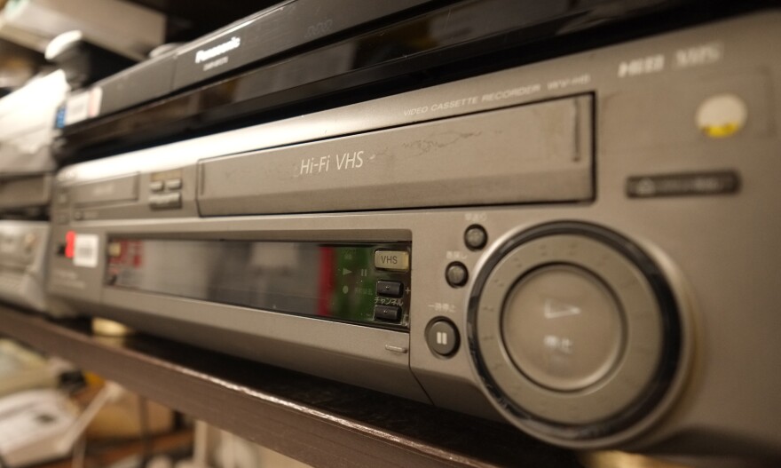 A close up of an old fashioned grey VCR on a shelf.