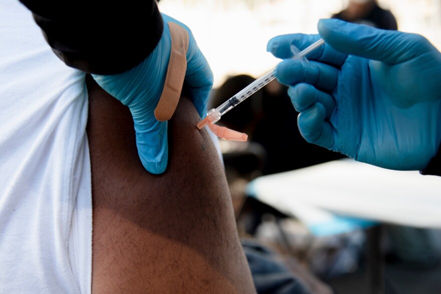 A gloved hand injects a COVID vaccine dose into a person's arm.