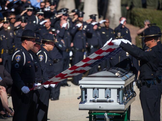 Riverside Police Officers fold an American flag over Michael Crain's coffin at the Riverside National Cemetery.