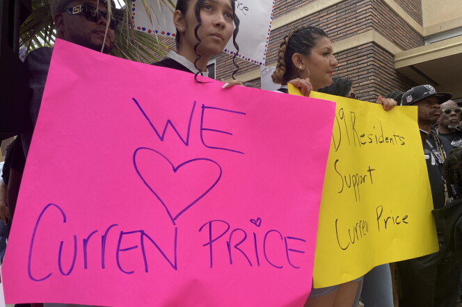 A woman is holding a pink sign that says we love Curren Price. She is in a crowd of people at a news conference where people called on the city council not to suspend Price, who is charged with public corruption.