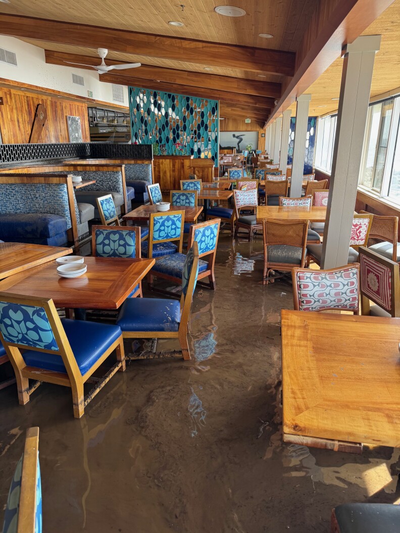 A restaurant dining room with natural lighting with several chairs and tables and booths. Muddy water is about a foot high on the ground.
