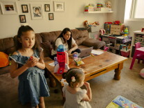 A woman looks at her laptop, while her two daughters play around her in the living room. 