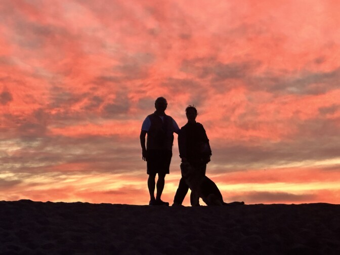 A man and woman backlit against a brilliant sunset at the ocean.