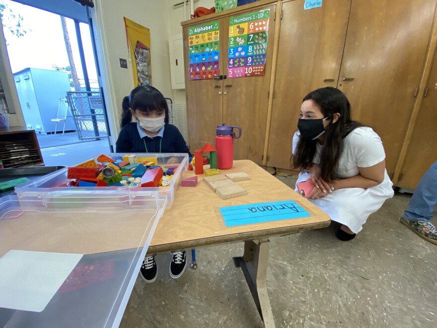 A transitional kindergartener at Harding Elementary in Sylmar plays with blocks as Kelly Gonez, president of the L.A. Unified school board, looks on. The student has been given her own set of toys; shared toys, materials and supplies are not allowed in L.A. Unified School District classrooms under reopening guidelines for hybrid instruction.