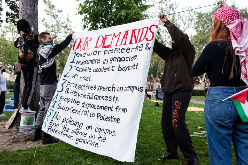 Several young people hold up a large white sign that reads "OUR DEMANDS".