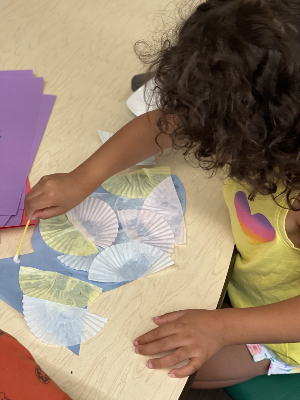 A child with medium-tone skin makes paper fans at a pre-school.