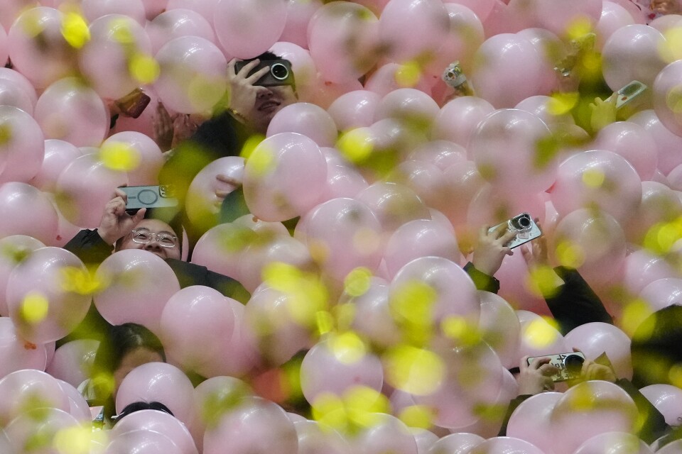 Falling balloons and confetti drop on people.