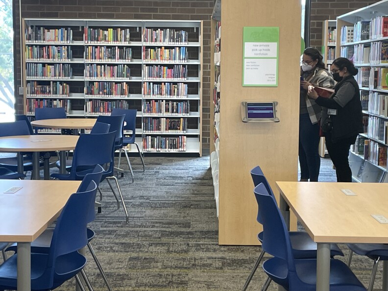 Library patrons browse through books on a shelf.