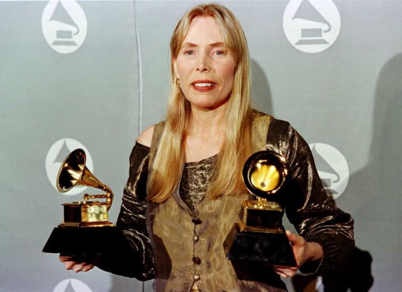 LOS ANGELES, UNITED STATES:  Joni Mitchell smiles as she holds two Grammy Awards at 38th Annual Grammy Awards 28 February in Los Angeles. Mitchell won Grammys for Best Pop Album for "Turbulent Indigo."   AFP PHOTO/Jeff Haynes (Photo credit should read JEFF HAYNES/AFP via Getty Images)