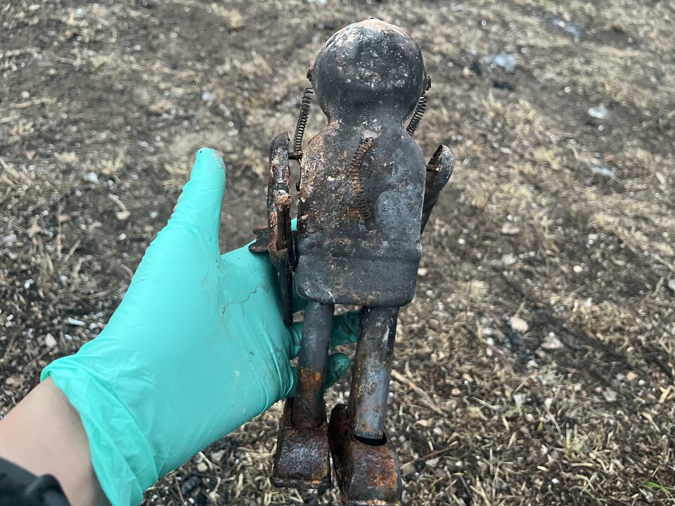 A gloved hand holds a charred tin robot