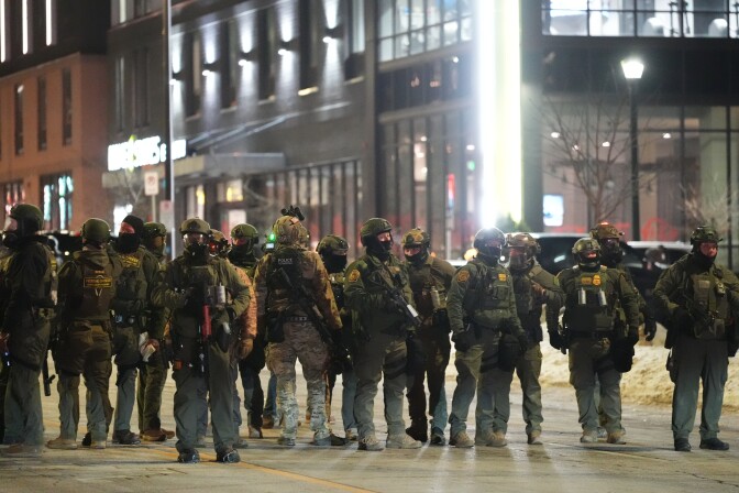 A row of people in heavy jackets stand on a city street.