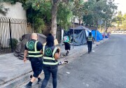 Four outreach workers from Urban Alchemy are walking down the street wearing all black and vests that identify them as part of Urban Alchemy, the nonprofit hired by Mitch O'Farrell's district to assist LAHSA with outreach. They are handing out food and water to unhoused people. 