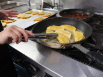 A arm is shown cooking tacos in a frying pan on a stove. 