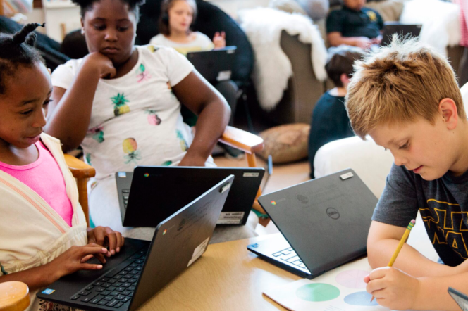 Children write and use laptops in a classroom.