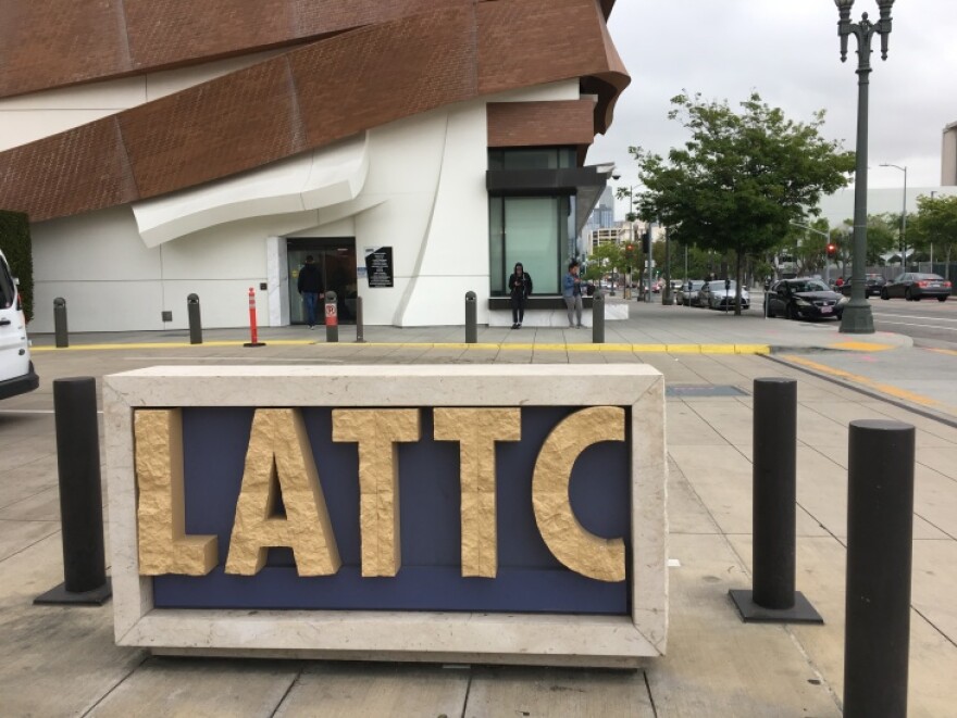 Three students wait outside a campus building at the intersection of two streets. In front of them, a large sign reads "LATTC."