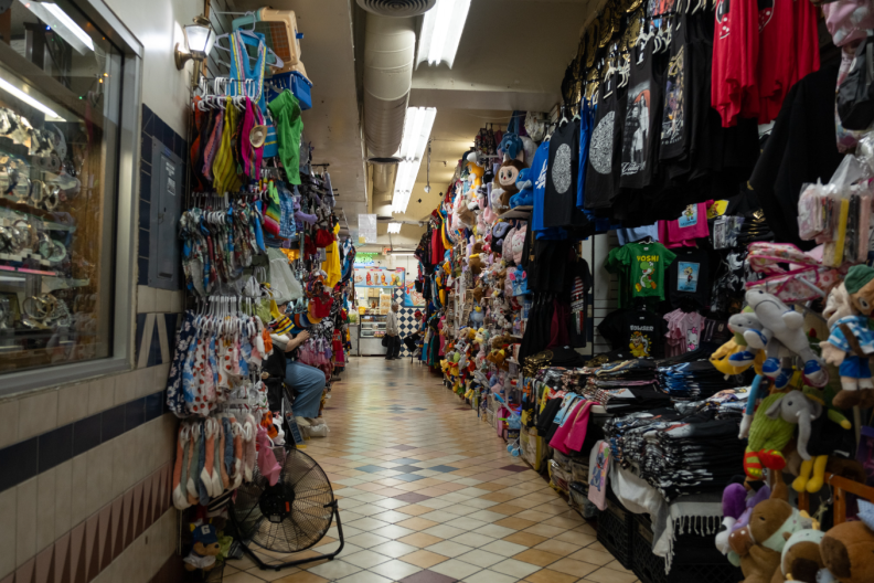 An almost empty hallway filled with vendors on both sides. Items in the stalls include t-shirts, toys, other clothing.