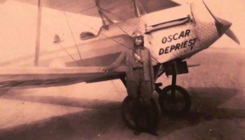 A sepia photograph of a dark-skinned woman, wearing an aviator uniform, standing next to a small plane