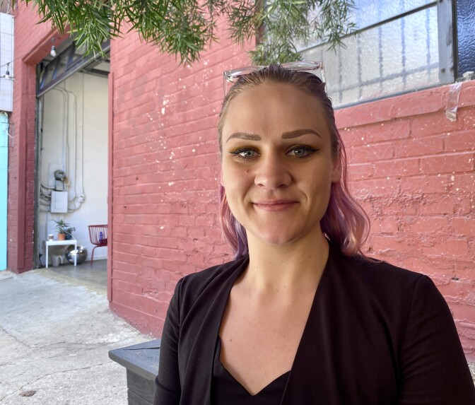 Sarah Fay is photographed wearing a black cardigan with a pair of glasses resting on top of her hair which is pulled into a ponytail.